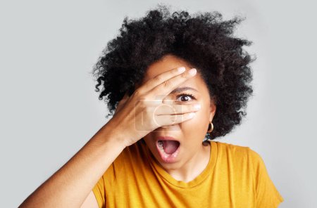 Surprise, wow and woman peeking through hand isolated on a white background in studio. Shocked, face and African female person shy, embarrassed or fear, scared or shame, emoji or mind blown portrait