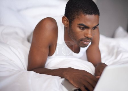 Photo for Black man, bed and relax with laptop for research, social media or networking in duvet or sheets at home. African male person or freelancer typing on computer and lying in bedroom for online search. - Royalty Free Image
