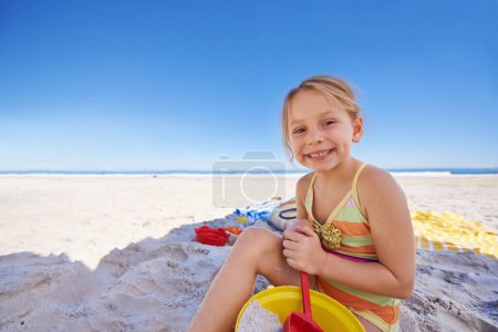 Foto de Feliz, retrato y niña con juguetes de playa para vacaciones lúdicas, vacaciones de verano o fin de semana al aire libre. Persona femenina, niño o niño pequeño que juega con sonrisa, cubo y pala en la arena o espacio de maqueta. - Imagen libre de derechos
