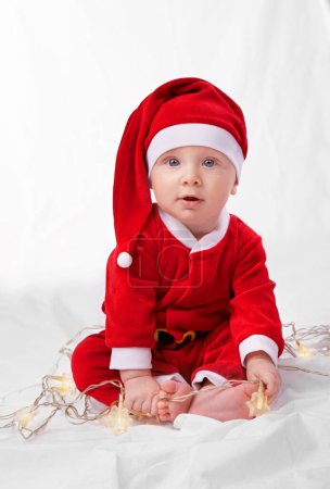 Photo for Baby, portrait and cute with santa costume for first Christmas holiday, star lights and white background. Boy toddler, xmas and outfit for festive season or celebration, innocent and adorable in hat - Royalty Free Image