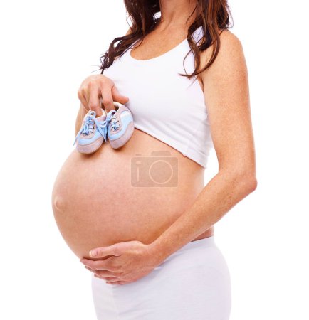 Foto de Mujer, embarazada y estudio con zapatos de bebé, maternidad y confianza con cuidado. Madre, orgullosa y embarazada con vientre, hijo y estómago para una crianza y maternidad positivas sobre fondo blanco. - Imagen libre de derechos