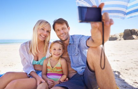 Téléchargez les photos : Famille heureuse, plage et détente avec selfie pour une photo, un moment ou une photographie en pleine nature. Mère, père et enfant avec le sourire pour la photo, appareil photo ou coller la mémoire ensemble sur la côte de l'océan. - en image libre de droit