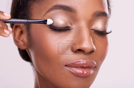 Photo for Black woman, face and brush for eyeshadow with makeup, beauty and lashes isolated on pink background. Skin glow, cosmetics product and tools for cosmetology, shimmer or glitter with shine in studio. - Royalty Free Image
