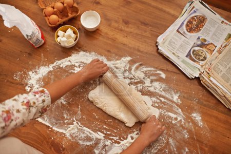 Téléchargez les photos : Pâte, recette et mains avec rouleau à pâtisserie sur la table, au-dessus de la cuisson dans la cuisine et gros plan sur le processus dans la boulangerie. Personne, préparer et presser le pain avec de la farine et préparer la semoule avec un guide d'information dans le livre. - en image libre de droit