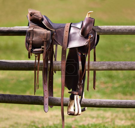 Téléchargez les photos : Selle, cheval et ferme sur une clôture de ranch, équitation et sports équestres à la campagne. Western, cow-boys et terrain au Texas, étrier et siège en cuir ou équipement pour l'exercice en plein air dans le paddock. - en image libre de droit