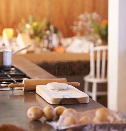 Foto de Masa, alfiler y tabla de madera en la cocina con ingredientes en el mostrador para hornear y cocinar con pastelería para pan con receta. Harina, trigo y patatas con estufa y olla para alimentos con verduras. - Imagen libre de derechos