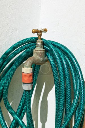 Photo for Tap, pipe and garden hose with attachment for water, pressure or environmental care at home. Closeup of faucet with plastic hosepipe rolled up on wall for liquid supply, service or outdoor gardening. - Royalty Free Image