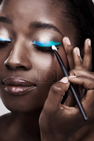 Téléchargez les photos : Brosse, maquillage et visage de femme noire avec des cosmétiques pour le bien-être, la beauté et le modèle. Cosmétologie, soins de la peau et personne avec des outils pour l'application de maquillage, fard à paupières bleu et produits en studio. - en image libre de droit