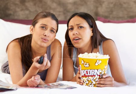 Photo for Television, remote control and confused women on a bed with popcorn, movie or film in their home together. Watching tv, face and friends in a bedroom with theatre snack for Netflix, video or show. - Royalty Free Image