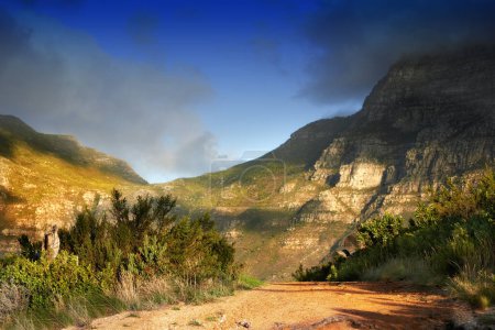 Foto de Montañas, naturaleza y nubes en el cielo para viajar, senderismo y turismo ecológico con camino de tierra, sendero o sendero. Antecedentes de medio ambiente, paisaje y arbustos en verano para la biodiversidad en Ciudad del Cabo. - Imagen libre de derechos