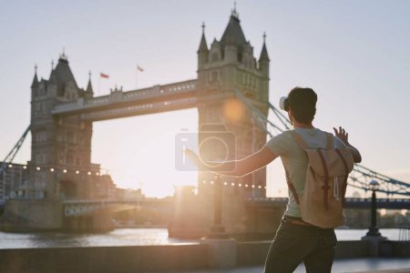 Téléchargez les photos : VR, jeux et l'homme en vacances à Londres pour Voyage, ai expérience et métaverse futuriste dans la ville. Europe, fantasme numérique et gamer avec des lunettes de réalité virtuelle 3D sur un pont en Angleterre. - en image libre de droit