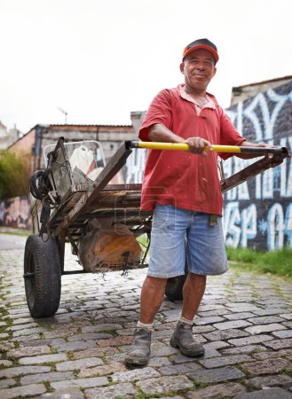 Foto de Hombre, retrato y carro de basura en la calle para sonreír, caminar y recoger basura para reciclar para la ecología. Persona, rickshaw o carretilla para la sostenibilidad, el medio ambiente y la favela en carretera en Sao Paulo. - Imagen libre de derechos