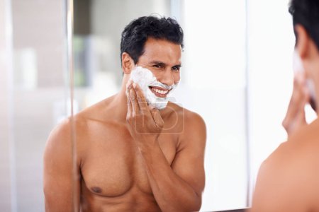 Téléchargez les photos : Homme, soin de la peau et mousse sur le visage dans le miroir de salle de bain pour le rasage, le toilettage et l'épilation. Sourire, cosmétiques et homme heureux pour le bien-être, le traitement du visage ou la routine matinale avec réflexion - en image libre de droit