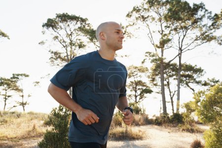 Foto de Fitness, running y hombre en camino en el bosque para la salud, el bienestar y el fuerte desarrollo corporal. Entrenamiento, ejercicio y corredor en la carretera en la naturaleza para el entrenamiento maratón, rendimiento y desafío matutino - Imagen libre de derechos