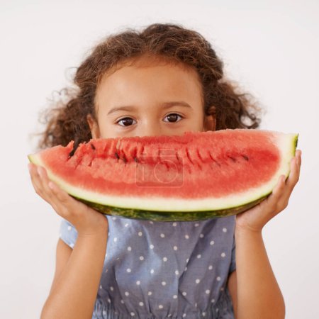 Portrait, eyes or girl with watermelon in studio for healthy, diet or wellness on grey background. Fruit, hiding or kid model face with gut health, nutrition or organic snack for digestion support.