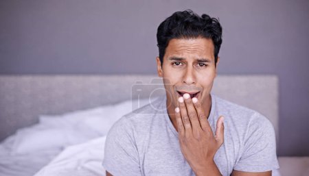 Photo for Man, yawn and tired in bedroom in portrait, fatigue and insomnia with sleep problem in morning. Young person, sleepy face or exhausted on break on lazy weekend, pyjamas or stress on bed in apartment. - Royalty Free Image