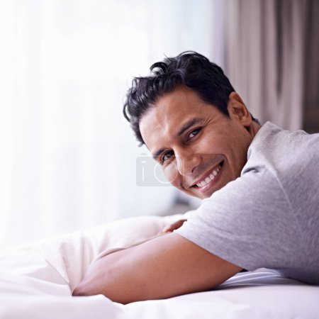 Photo for Man, happy and calm in bedroom in portrait, wellness and confident person on morning in home. Young guy, positive face and healthy on break on lazy weekend, pyjamas and satisfied on bed in apartment. - Royalty Free Image