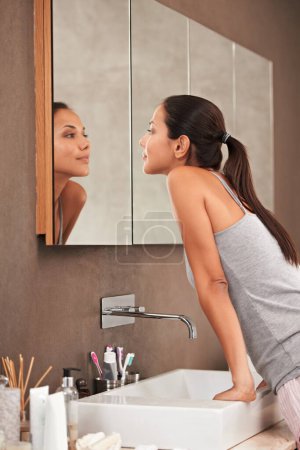 Photo for Bathroom, mirror and woman check face for skincare, beauty and wellness in morning routine. Health, dermatology and person in reflection for pimple, acne or cleaning, hygiene and grooming at home. - Royalty Free Image