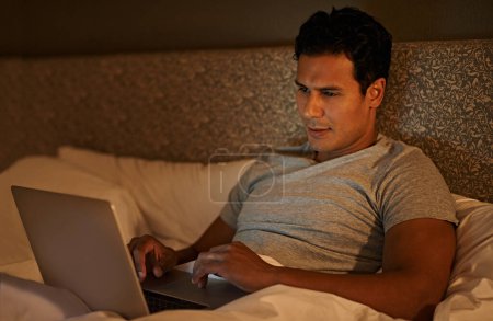 Téléchargez les photos : Homme, heureux et ordinateur portable dans la chambre à coucher la nuit, abonnement en ligne et film en streaming à regarder le week-end. Personne calme, se détendre et ordinateur sur le lit dans la couette, bien-être et défiler sur les médias sociaux à la maison. - en image libre de droit
