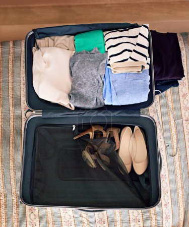 Photo for Travel, luggage and clothes in suitcase for holiday or vacation packing in bedroom from above. Adventure, bag and journey with clothing on bed in apartment, hotel or lodge for weekend getaway. - Royalty Free Image