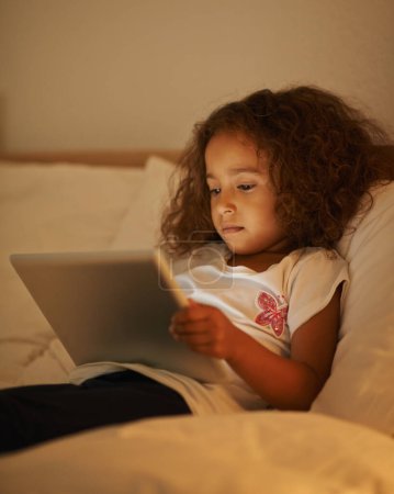 Photo for App, child and tablet in bed at night, comfortable and online for games or playing in home. Female person, girl and movie in bedroom or lying to relax, website and internet or streaming entertainment. - Royalty Free Image