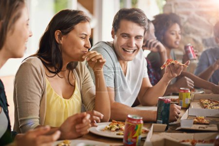 Téléchargez les photos : Amis, rire et manger de la pizza à la maison avec bonheur, soda et rassemblement social pour coller dans la salle à manger. Les hommes, les femmes et la restauration rapide avec une blague drôle et la diversité à la table dans le salon de la maison. - en image libre de droit
