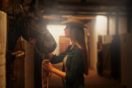 Téléchargez les photos : Cowgirl, heureuse et femme avec cheval à la grange ou à l'écurie au Texas pour les loisirs. Western, animal et sourire de la personne au ranch avec animal de compagnie ou étalon pour passe-temps avec soin pour le bétail à la ferme équestre. - en image libre de droit