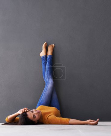 Téléchargez les photos : Femme, style et fond mural pour la pose, les pieds et la détente sur le sol dans le sommeil avec la mode. Femme, positive et cool à la maison pour le bonheur, décontracté et bien-être en jeans avec les orteils dans l'air. - en image libre de droit