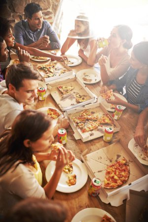 Foto de Grupo, amigos y fiesta con merienda, pizza y diversidad para la alegría o la diversión con la juventud. Hombres, mujeres y comida rápida con bebida, reunión social y celebración para el almuerzo o ángulo alto en la pizzería italiana. - Imagen libre de derechos
