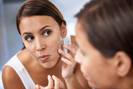 Photo for Pimple, woman and skincare in mirror with pores or face spot or acne on cheek. Home, female person and serious with reflection in bathroom for skin and self care as daily routine for treatment. - Royalty Free Image