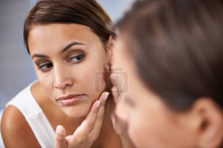 Téléchargez les photos : Pores, femme et soins de la peau dans un miroir avec tache faciale ou bouton ou acné sur la joue. Femme, pointant et sérieux avec réflexion dans la salle de bain pour la peau et l'auto-soin comme routine quotidienne pour le traitement. - en image libre de droit