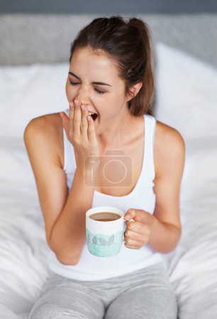 Photo for Woman, fatigue and yawning with tea in bed, waking up from sleeping or nap with morning routine at home. Insomnia, tired and sleepy in bedroom, warm drink or beverage for breakfast and start day. - Royalty Free Image