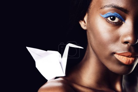 Photo for Black woman, portrait and makeup with cosmetics, fine art and origami bird or dove on a dark studio background. Closeup or face of African female person or model with beauty eye color on mockup space. - Royalty Free Image