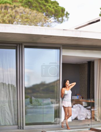 Photo for Woman, balcony and waking up with coffee on pajamas in morning, fresh and healthy on bedroom in Los Angeles. Glass door, female person and happy with thoughts to relax for leisure, comfort and enjoy - Royalty Free Image