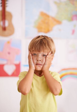 Child, boy and hands on face for stress or worry in playroom, anxiety with serious facial expression and fear. Scared, concern or unhappy with fail or mistake, negative reaction for crisis or problem.
