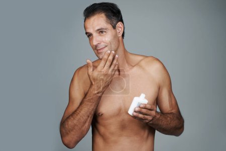 Photo for Man, moisturizer and skincare lotion in studio for hygiene treatment for facial wellness, grey background or mockup space. Male person, product and healthy dermatology for anti aging, cream or apply. - Royalty Free Image