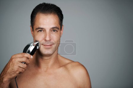 Photo for Man, portrait and razor for shaving or grooming skincare for electric tool or dermatology, trimmer or grey background. Male person, face and hair removal for beard routine, mockup space or studio. - Royalty Free Image