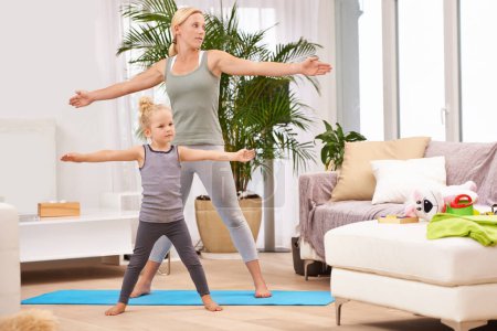 Téléchargez les photos : Yoga, exercice avec la mère et la fille dans le salon, étirant les bras pour l'équilibre et la liaison. Femme, jeune fille et fitness ensemble à la maison familiale, santé et bien-être avec amour et soin. - en image libre de droit