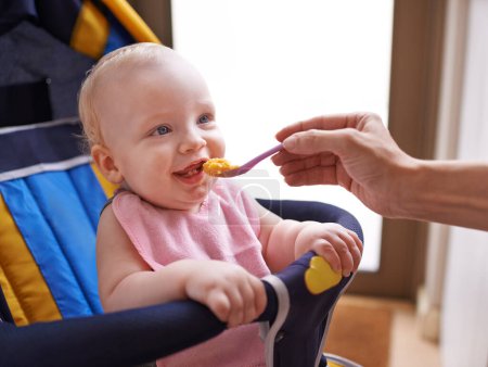 Photo for Baby, hand and feeding food with spoon in chair for nutrition porridge for fiber vitamins or childcare, morning or breakfast. Kid, person and eating meal in home or development growth, dinner or care. - Royalty Free Image