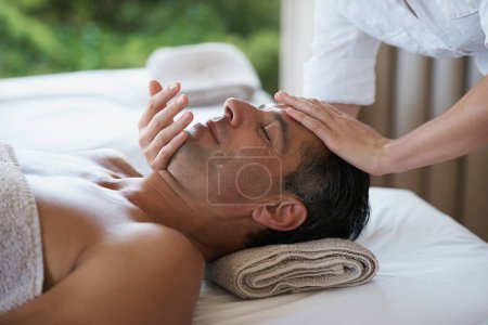 Photo for Relax, face massage and man at salon for skincare, peace and calm at luxury resort at table for wellness. Beauty, therapy and masseuse at spa for head treatment, health and hands of person pampering. - Royalty Free Image