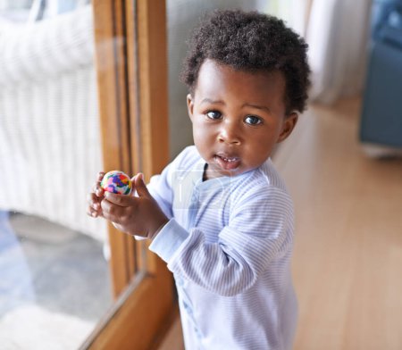 Foto de Bebé, retrato y pelota jugando en casa para el crecimiento del desarrollo en apartamento para juegos, bienestar o infancia. Persona negra, niño y la cara en la ventana de la casa en Kenia en el niño pequeño, diversión, guardería o salud. - Imagen libre de derechos