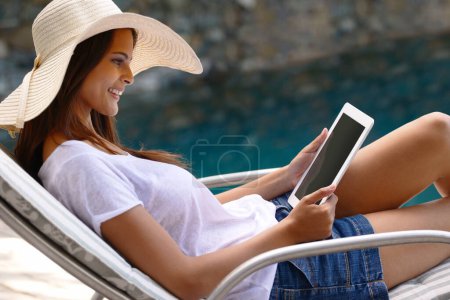 Photo for Holiday, vacation and woman at pool with tablet, hat and relax with happy summer travel on hotel patio. Lounge, digital app and girl with smile, reading and ebook with sunshine, technology and luxury. - Royalty Free Image