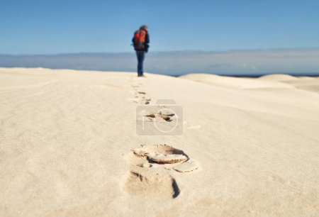 Photo for Person, hiking and walking on sand dunes for fitness adventure in desert and extreme sport in arid climate. Athlete, back or survival gear for nature exploration, footprints or wanderlust vacation. - Royalty Free Image