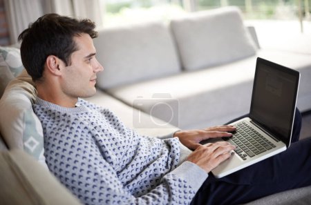 Photo for Man, laptop and sofa in living room for tech, social media and research for home or indoor on weekend. Male person and smile with hand on keyboard for browse, type and screen with internet and online. - Royalty Free Image
