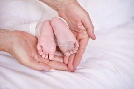 Photo for Baby, feet and hands for childcare on bed or development with parenting trust with support, love or connection. Kid, foot and fingers in palm for wellness bonding in apartment, protection or security. - Royalty Free Image