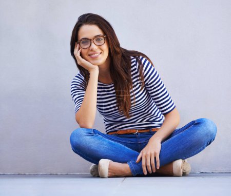Photo for Happy, fashion and portrait of woman on floor with wall background for casual or trendy style. Smile, model and relax with confident young person legs crossed in glasses for casual clothing outfit. - Royalty Free Image