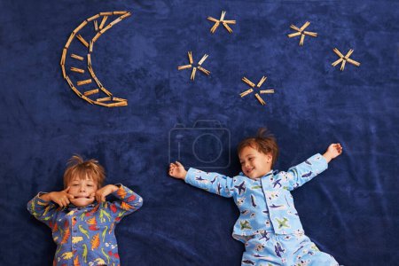 Foto de Sonríe, juega y niños con cara divertida para la noche, la luna y las estrellas de la alfombra. Felicidad, vista superior y hermanos para la expresión facial juguetona, el crecimiento y el desarrollo de la infancia en el suelo del dormitorio. - Imagen libre de derechos