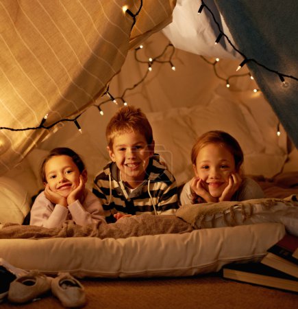 Photo for Kids, happy and playing in blanket fort with portrait for fantasy, bonding and fairy lights at night. Friends, children and face with smile for pajama party, sleepover and pillow tent with lighting. - Royalty Free Image