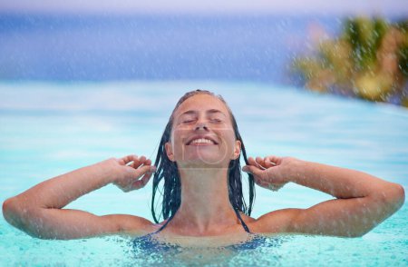 Photo for Face, smile and rain with woman in swimming pool for travel, holiday or vacation as tourist. Relax, water and wellness with happy young swimmer person outdoor at tropical resort for getaway trip. - Royalty Free Image