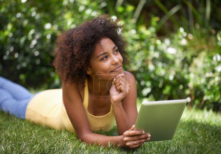 Téléchargez les photos : Femme africaine, tablette et se détendre sur l'herbe avec la pensée, la mémoire et sourire pour poster sur le blog web. Fille, écran tactile numérique et heureux dans la cour, jardin et en plein air avec application pour les médias sociaux au Brésil. - en image libre de droit